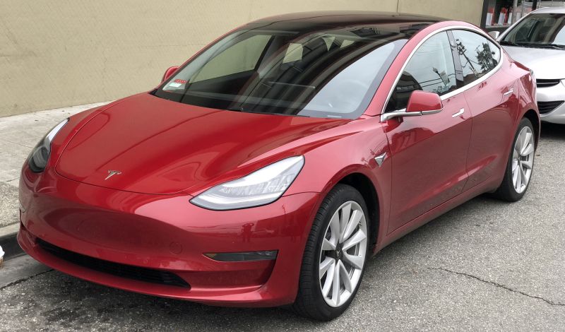 Red Tesla Model 3 parked on street.